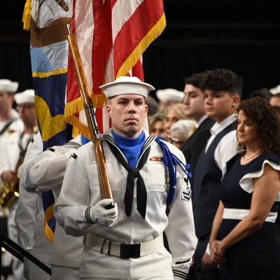 Navy Sailors in uniform parade the American and Navy flags.