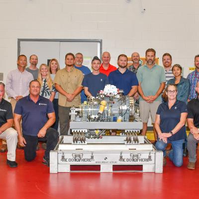 Fleet Readiness Center East (FRCE) and Rolls Royce personnel pose for a group photo with a fully assembled lift fan clutch for the F-35B Lightning II aircraft. FRCE personnel became the first within the Department of Defense (DoD) to perform a successful assembly of this component outside of Rolls Royce’s LiftWorks facility in Indianapolis.