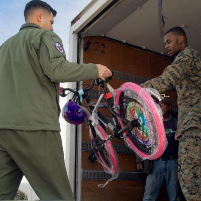 Man handing another man a children's bike with pink tires. 