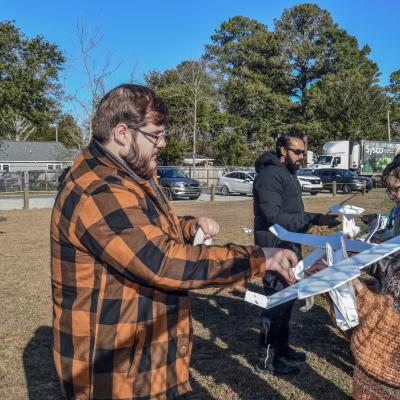 Man stands on the left helping female student on the right with foam airplane