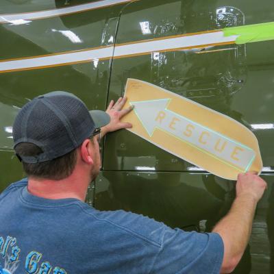 Man applying "rescue" arrow to side of green aircraft