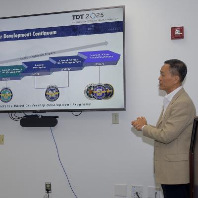 Man standing in front of a large screen monitor using PowerPoint slides while speaking. 