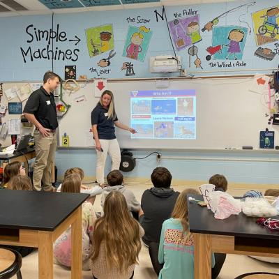Two adults show presentation to students sitting on floor in classroom 