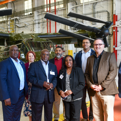 Eight individuals stand in front of a green V-22 aircraft