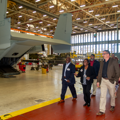 eight individuals walk on a red pathway next to the rear of an aircraft 