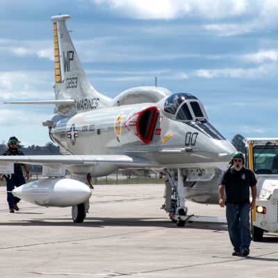 Man walking in front of aircraft and small metal vehicle 