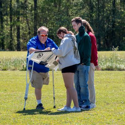 Three students stand with a gentleman on crutches outside 