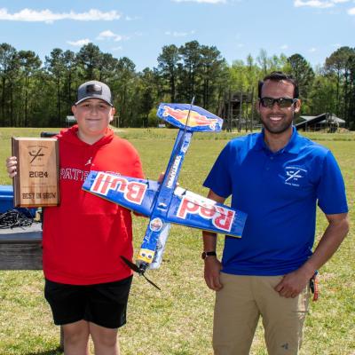 Student holds model aircraft and plaque next to a gentleman in blue 