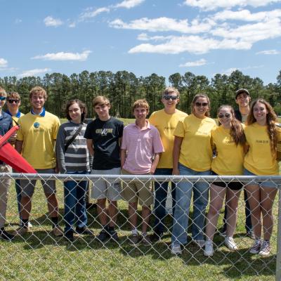 Team of students wearing yellow stand outside with trophy and model aircraft
