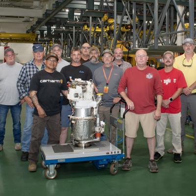Artisans at Fleet Readiness Center East’s (FRCE) Engine Driven Compressor and Gas Turbine shop stand for a group photo with a freshly overhauled auxiliary power unit for the F/A-18E/F Super Hornet. FRCE recently achieved a significant production milestone by eliminating high-priority backorders for auxiliary power units used in the Super Hornet, bolstering the platform’s mission readiness. 
