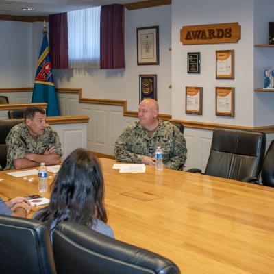 Five individuals speaking while sitting at a table  