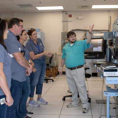 Five people standing with one showing the others a machine