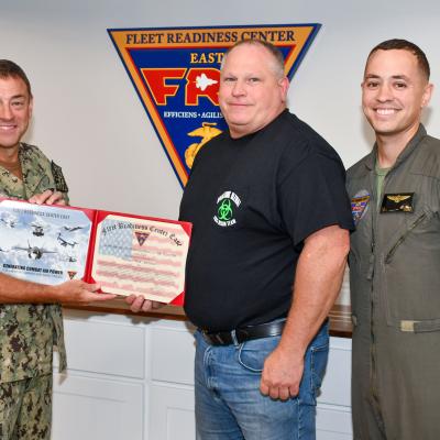 Three men smile at camera while two hold an award