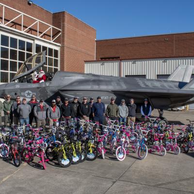 Group of people stand in front of aircraft with lots of children's bikes