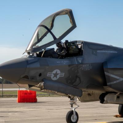 Tet pilot sits in cockpit of F-35B Lightning II aircraft with open canopy as ground crew stands by.