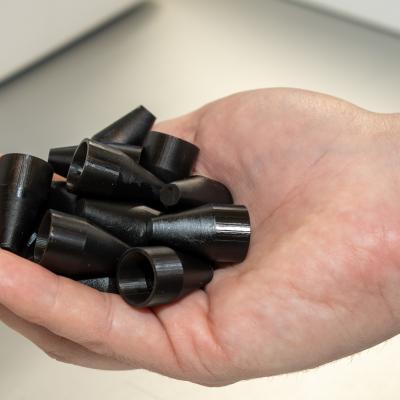 Close-up image of a man's hand holding several small, black polymer cones 3D printed as a maintenance aid for F-35 Lightning II aircraft