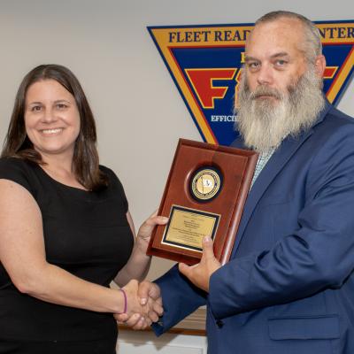Man and woman shaking hands while holding award plaque