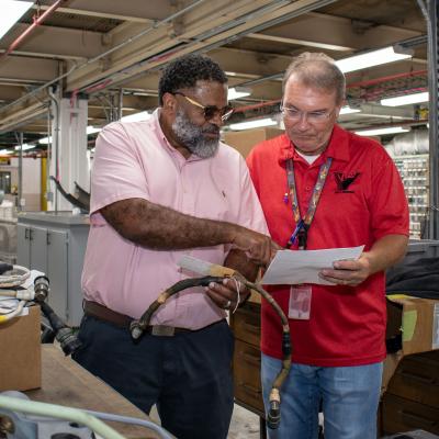 Man in pink shirt shows man in red shirt something on paper 