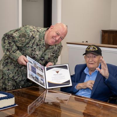 Man in military uniform holds up award with elderly man 