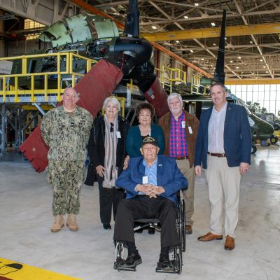 Group of people pose for photo in front of aircraft in aircraft hangar
