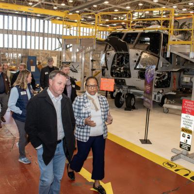 Group of people walk along a red isle in front of military aircraft inside aircraft hangar