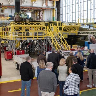 Vertical photo of group of people standing in front of V-22 during maintenance in aircraft hangar