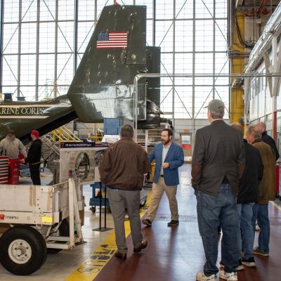 Group of people in aircraft hangar looking at the tail end of a V-22 Osprey