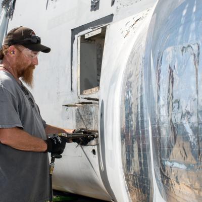 Man in grey shirt works on sheet metal on military aircraft exterior 