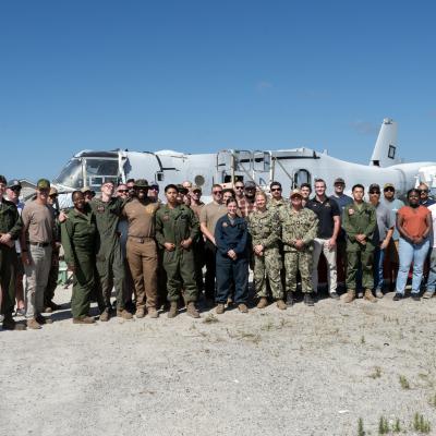 Group of civilians and service members pose for group photo in front of military aircraft