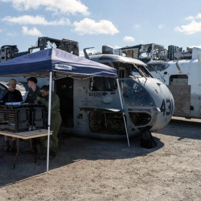 Three people stand under tent near two military aircraft 