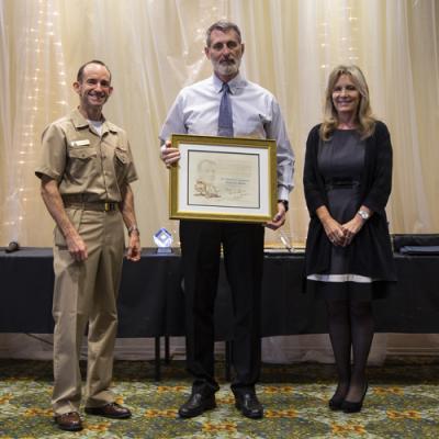 Mark Keenan accepts the Dr. Charles C. Lauritsen Memorial Award from Rear Adm. Scott Dillon, NAWCWD commander, and Joan Johnson, NAWCWD executive director, during the 2019 Honorary Awards Ceremony at China Lake on June 25. (U.S. Navy photo by Ryan Smith)