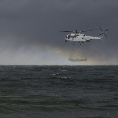 Helicopter hovering over open ocean carrying an inflatable boat