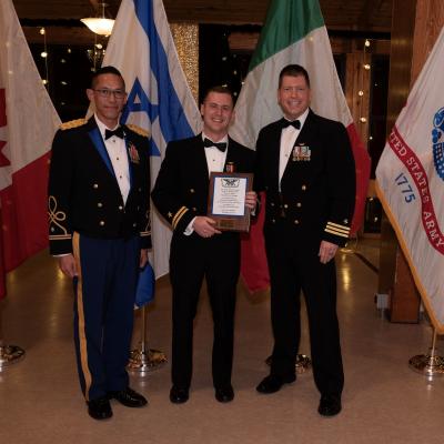 Three military officers pose for a photo in front of international flags.
