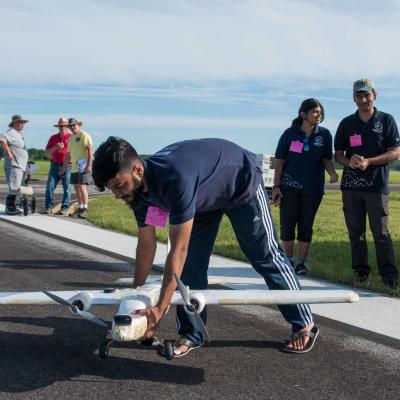 A student sets their small unmanned system on the flight line joined by his teammates and competition volunteers in the background.