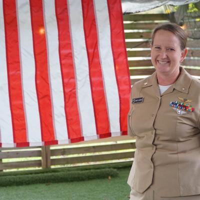 Naval officer in khaki uniform standing in front of American flag