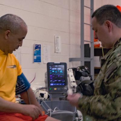 A uniformed Navy audiologist takes vital sign readings for another sailor.