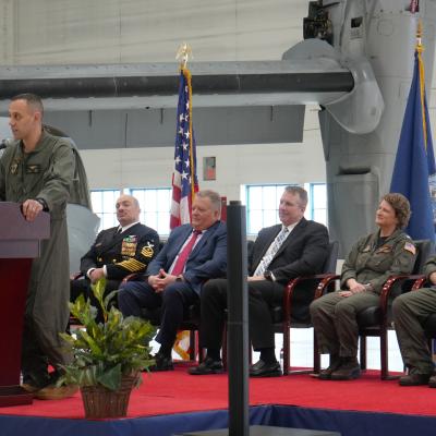 The HX-21 commander speaks at a podium during a change of command ceremony.
