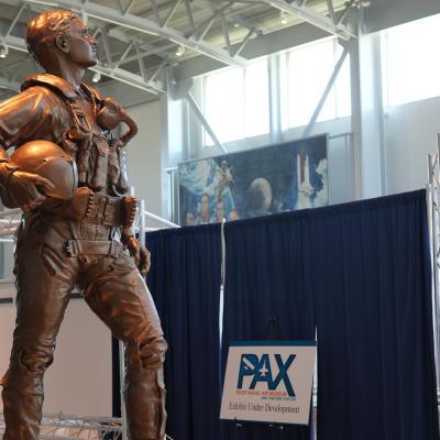 A bronze statue of a test pilot stands in front of a curtained museum exhibit under construction.