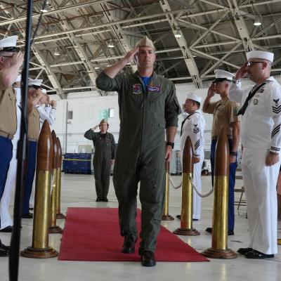 A military officer salutes during a change of command ceremony in an aircraft hangar.