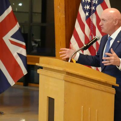 A speaker gives remarks at a podium in front of flags.