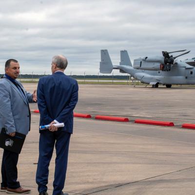 Three men stand outside in front of a military aircraft