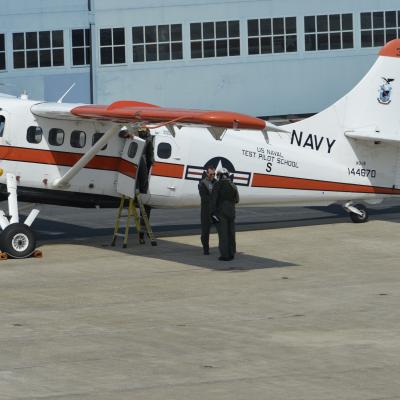 Cmdr. Jeremy DeBons shakes hands with Lt. Col. Rory Feely in front of the school's NU-1B Otter aircraft.
