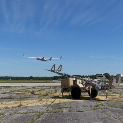 An RQ-21 Blackjack fixed-wing unmanned aerial system launches into blue skies over an airfield.