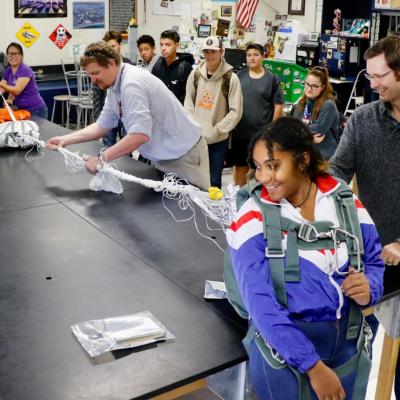 Jennifer Lam (in purple), Michael Petersen and Frederick Henderson attach a parachute to a Burroughs High School student and explain the intricacies of that during the BHS STEM day Nov. 8. (U.S. Navy photo by Paul Kakert)