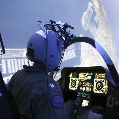A pilot operates a simulator surrounded by screens inside NAWCAD's Joint Simulation Environment.