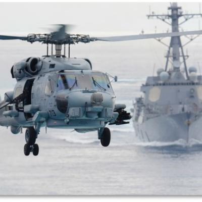 An MH-60 helicopter flying over a DDG in open ocean