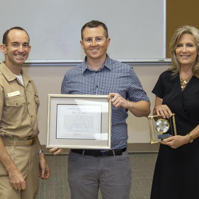 Rear Adm. Scott Dillon, left, NAWCWD commander, and Joan Johnson, right, NAWCWD executive director, pose with Dr. Manuel A. Garcia Memorial Award winner Ryan Baker during the Honorary Awards Ceremony in Point Mugu, California, on June 27. Award recipient James Bender was unable to attend. (U.S. Navy photo by Rob Grabendike)
