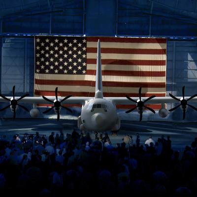 Artist rendering of a four propeller airplane in front of the USA flag in a hanger