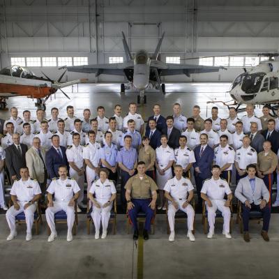 Test pilots, flight officers, and engineers under instruction from U.S. Naval Test Pilot School Class 166 pose for a class photo in the school's hangar.