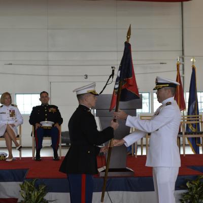 Lt. Col. Matthew Baumann takes a command flag from Cmdr. Daniel short in an aircraft hangar.